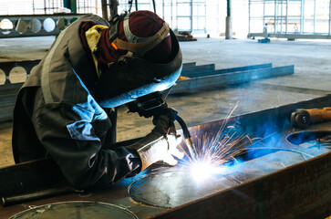 Craftsman welding steel structure h-beam with sparks fly from gas machine in fabrication factory.