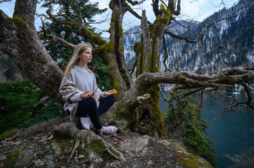 Naklejka na ściany i meble Girl sits on a tree and meditates near lake Ritsa in Abkhazia