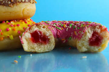 Yellow pink chocolate donuts lie a stack of a row of cut-off bitten doughnut stuffed with pink chocolate on a blue bright background with room for text. still life from food