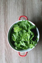 Bowl of lettuce on wooden table. Flat lay.