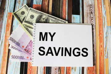 text MY SAVINGS written on a notepad, next to euro and dollar banknotes on a striped background, The concept of identifying leaks in expenses to fix them and increase savings