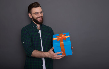 Happy young handsome bearded man in casual wear in good mood with big gift box in his hands having fun and posing over gray background