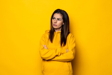 Portrait of an upset young woman dressed in sweater standing isolated over yellow background, holding arms folded