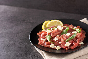 Marbled beef carpaccio on black plate on black stone. Copy space