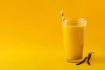 Delicious vanilla milkshake in glass on yellow background. Copy space