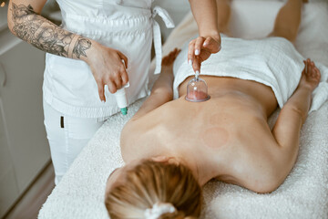 Obraz na płótnie Canvas professional female specialist is doing cupping therapy on the back of beautiful caucasian lady