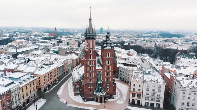 Drone footage of the red brick St Mary's Basilica (Mariacki Church) with two prominent towers in the Main Market Square of Krakow, Poland. Footage is made during the daytime. Clear white sky in he