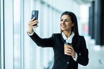 Business woman take selfie on phone holding coffee to go working at office