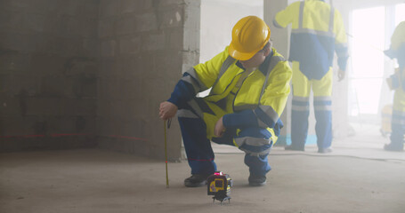 Manual worker using laser level machine and measuring tape in renovation room