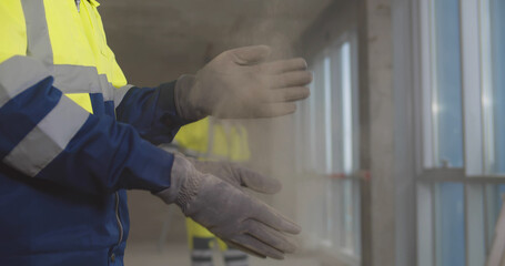 Close up of builder shaking off dust from gloves at construction site