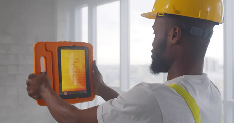 African builder doing analysis of heat on wall with thermal imaging camera