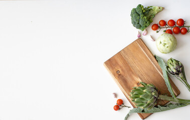 Artichoke on wooden cutting board. Vegetables on white background with garlic and cherry tomatoes....