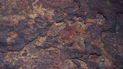 The dark rough texture of the stone with peeling rusty fragments. Background