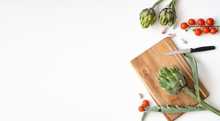 Artichoke on wooden cutting board. Vegetables on white background with garlic and cherry tomatoes. Concept very healthy food rich vitamins. How to cook and eat? Banner. Space for text.