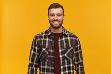 Fototapeta premium Portrait of happy handsome young bearded man in checkered shirt looks confident standing and looking at camera over yellow background