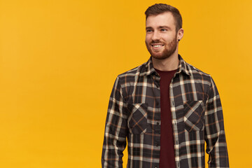 Smiling attractive young man in plaid shirt with beard standing and looking away to the side over...