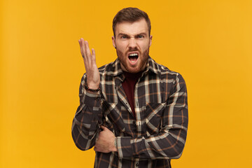 Furious angry young man in plaid shirt with beard and raised hand looks aggressive shouting and...