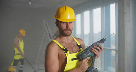 Young handsome male construction worker posing seductively shirtless holding drilling machine