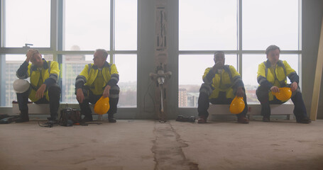 Tired team of builders sitting on heaters and resting at construction site