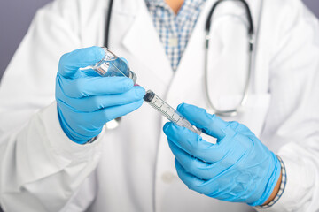 Doctor wearing a white uniform, medical gloves holding a syringe, and vaccine bottle preparing for injection vaccination. Vaccine for immunization, and treatment from coronavirus infection