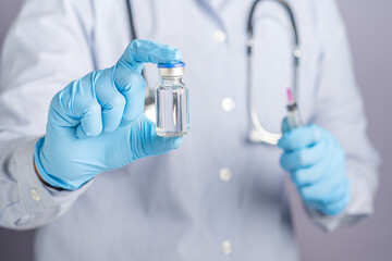 Doctor hand holding of a vaccine bottle and syringe against a gray background. Vaccine for immunization, and treatment from virus infection. Concept of medical and the fight against the virus