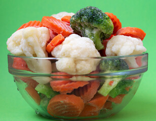 Frozen vegetables broccoli and carrots in a glass plate on a green background.