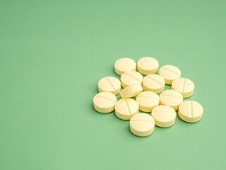 Pile of light yellow tablets medicine for people's health to heal diseases isolated on a green background. Space for text. Side view. Healthcare and medical concept