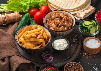 French fries, fried meat, pita bread, vegetables and spices on a dark background. A full meal or ingredients for shawarma, burrito, gyros. Close-up.