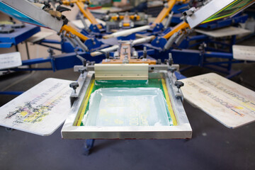 Serigraphy silk screen print process at clothes factory. Carousel Frame, squeegee and plastisol...