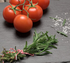 fred tomatoes and fresh sprig of rosemary with green leaves on a black background