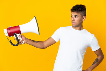 Young brazilian man isolated on yellow background holding a megaphone with stressed expression