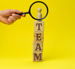 wooden figurine of a man on a pedestal and a hand with a magnifying glass on a yellow background....
