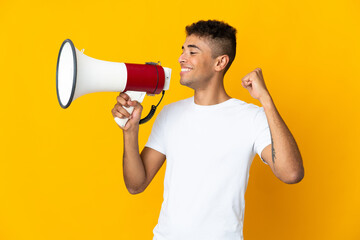 Young brazilian man isolated on yellow background shouting through a megaphone to announce...