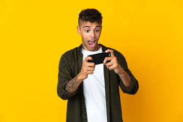 Young brazilian man isolated on yellow background playing with the mobile phone