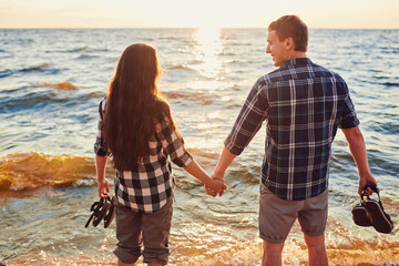 Happy caucasian fashionable couple in love holding hands and walking on coast near river.