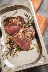 Rinder Steak medium rare gebraten mit Rosmarin und Salz auf Edelstahl Schale und Holzbrett und Stein Hintergrund dunkel