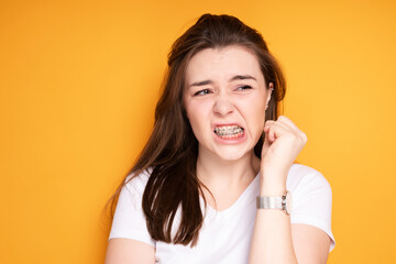 Girl in braces clenches her hand into a fist and frowns irritably with pain clenching her teeth