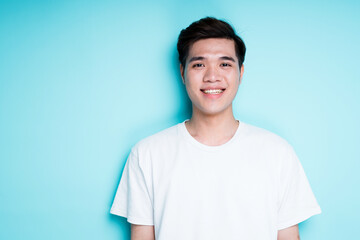 Young handsome vietnamese man in t-shirt smiling broadly while standing against blue background