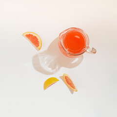 A jug of grapefruit juice with pieces of grapefruit around on a white background. A refreshing summer fruit citrus concept with minimal composition. Flat lay.