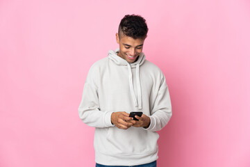 Young Brazilian man isolated on pink background sending a message with the mobile