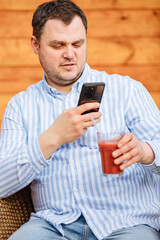 Man photographs his glass of red smoothie with the mobile phone. Food blogger posts photos with his juice glass. Propagating a healthy lifestyle on the Internet 