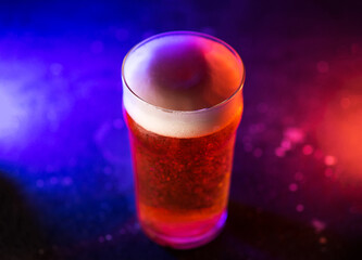 A glass of craft light beer on a dark background, colored trend light