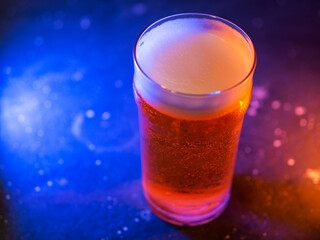 A glass of craft light beer on a dark background, colored trend light