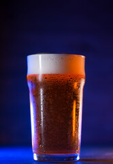 A glass of craft light beer on a dark background, colored trend light