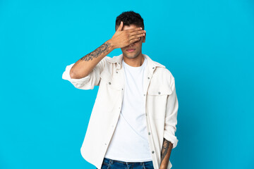 Young Brazilian man isolated on blue background covering eyes by hands. Do not want to see something