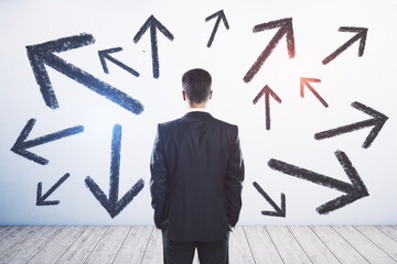 Businessman standing puzzled in front of a wall with multiple black arrows pointed in different directions. Decision making and career path concept