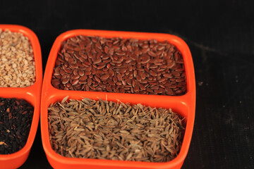 brown flax seed with cumin seeds in oregon bowl,indian spice mix in one plate,organic Flax seeds in ceramic orenge plate with caraway seeds, Cumin seeds in plate