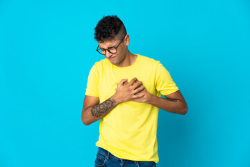 Young Brazilian man isolated on blue background having a pain in the heart