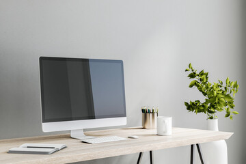 Modern computer monitor on wooden table with white keyboard, notebook and coffee mug on light grey...