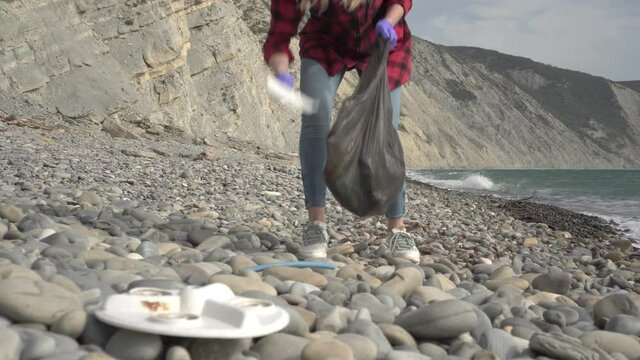 A woman cleans the sea shore from garbage. Volunteer ecologist person removes rubbish on the beach